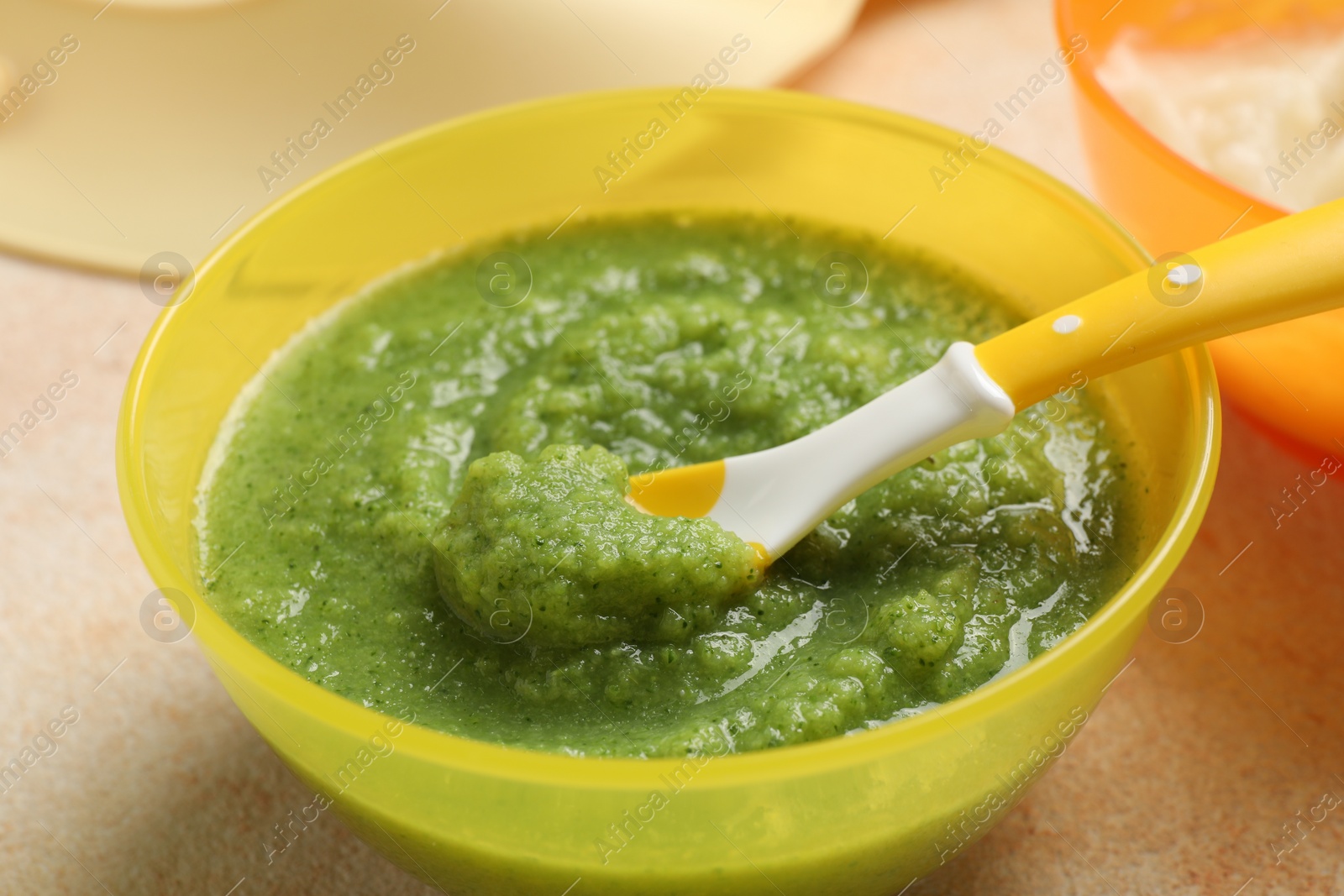 Photo of Baby food. Bowl with tasty broccoli puree on beige textured table, closeup