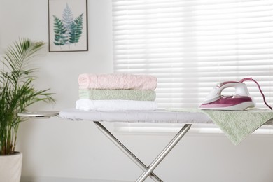 Photo of Modern iron and clean towels on board indoors