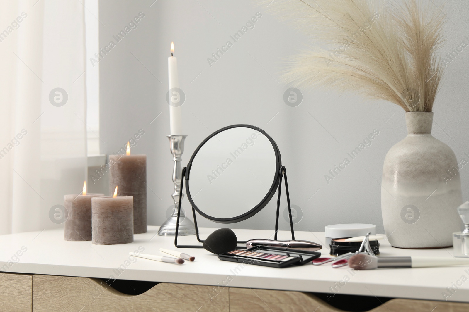 Photo of Dressing table with mirror, cosmetic products and burning candles in makeup room