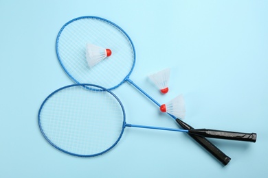 Photo of Rackets and shuttlecocks on light blue background, flat lay. Badminton equipment