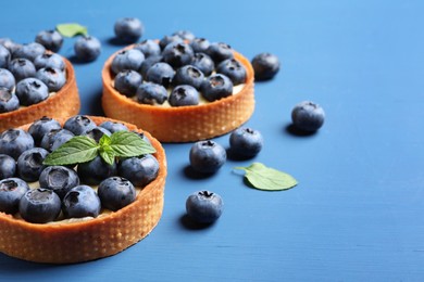 Tartlets with fresh blueberries and mint on blue table, space for text. Delicious dessert