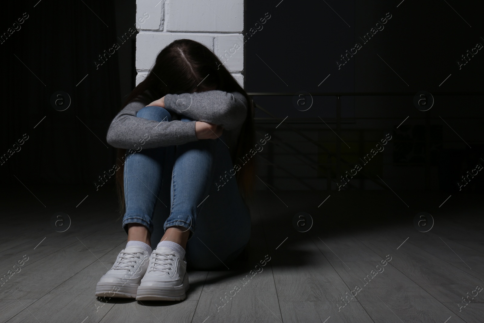 Photo of Upset teenage girl sitting at column indoors. Space for text