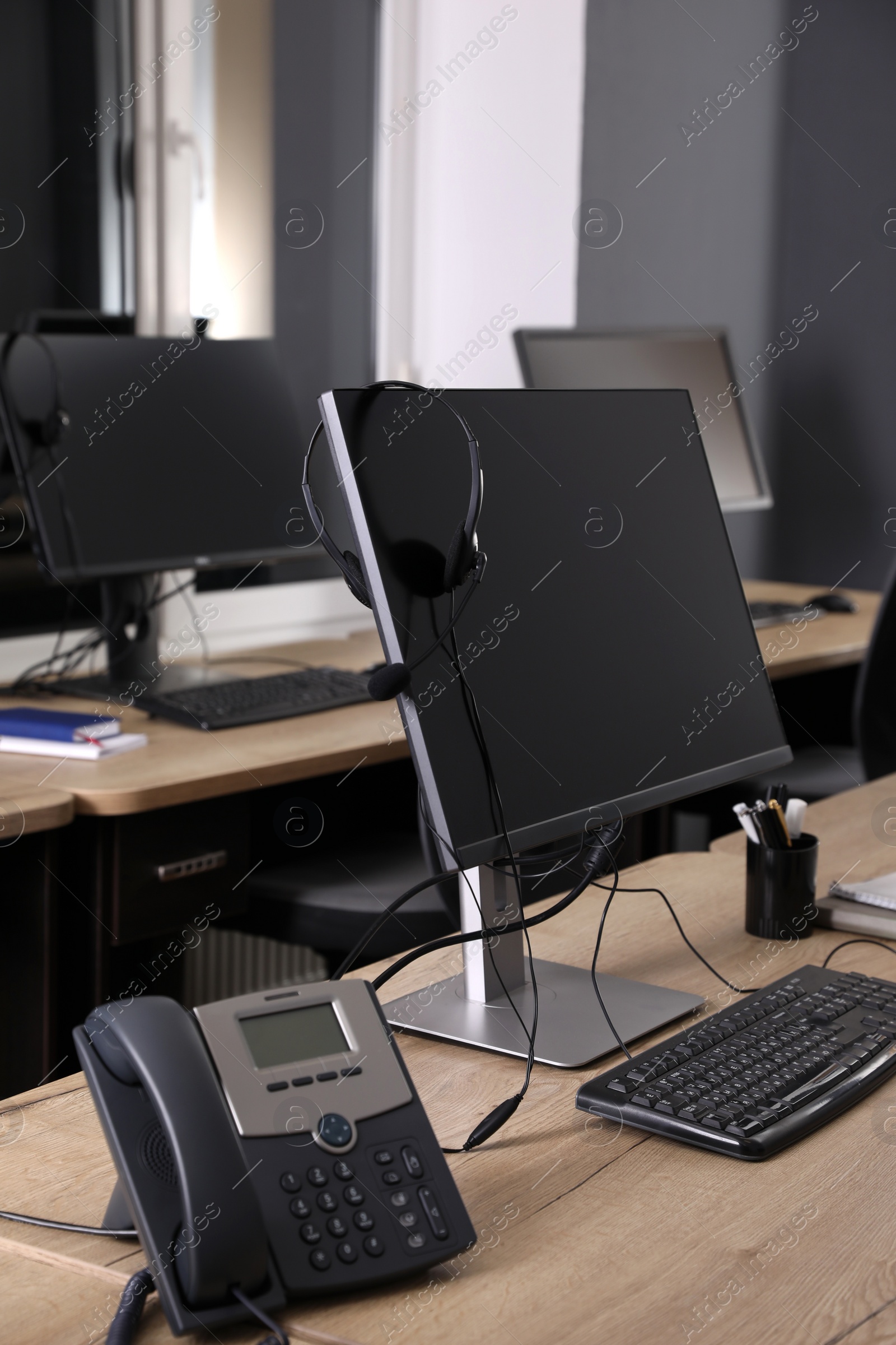 Photo of Modern computer with headset and stationary phone on wooden desk in office. Hotline service
