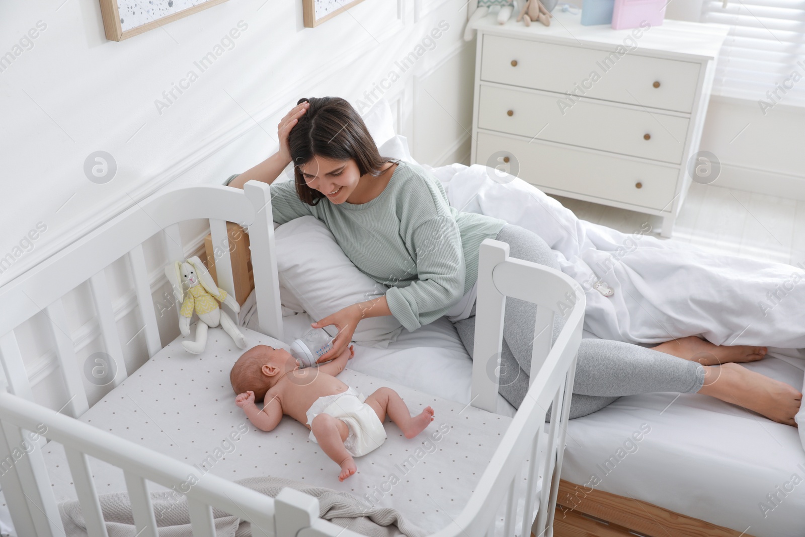 Photo of Happy young mother feeding her newborn baby from bottle at home