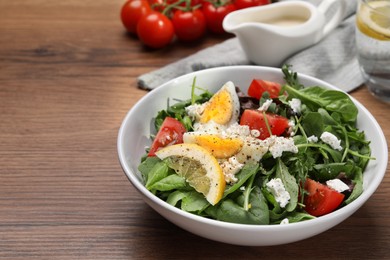 Delicious salad with boiled egg, tomatoes and cheese in bowl on wooden table, closeup. Space for text