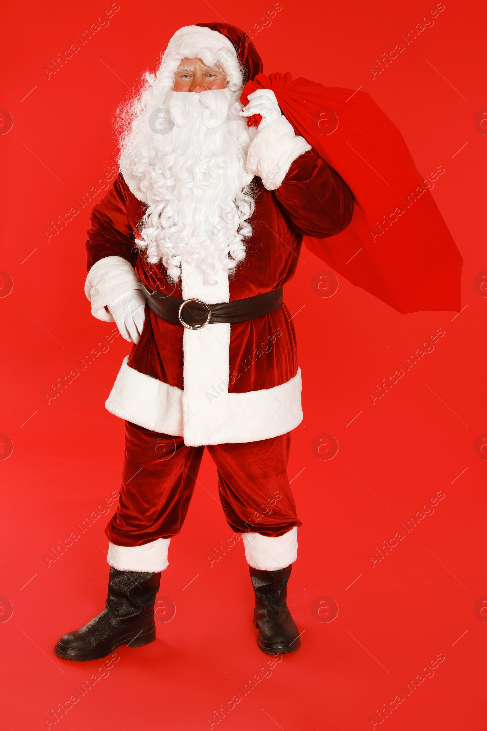 Photo of Authentic Santa Claus with bag full of gifts on red background