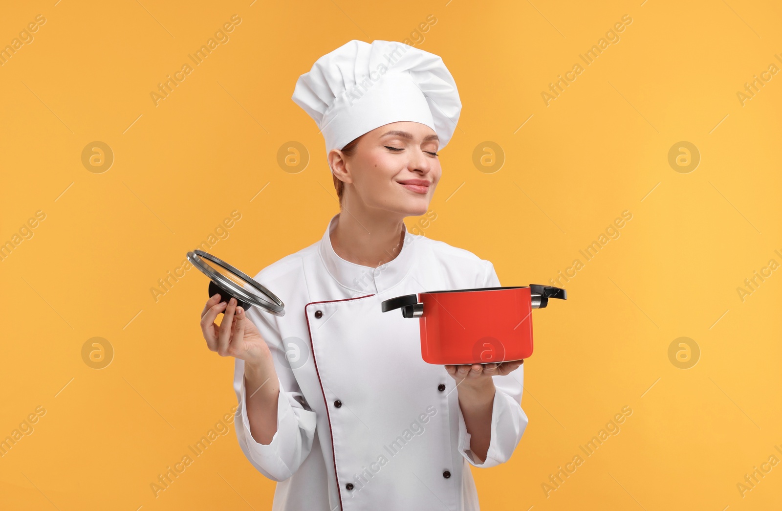 Photo of Happy chef in uniform holding cooking pot on orange background