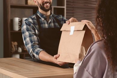 Photo of Worker giving paper bag to customer in cafe, closeup