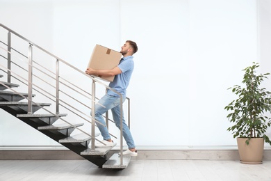 Young man carrying carton box upstairs indoors. Posture concept