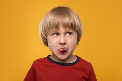 Photo of Cute boy showing his tongue on orange background