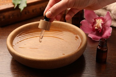 Photo of Woman dripping essential oil into bowl at wooden table, closeup. Aromatherapy treatment