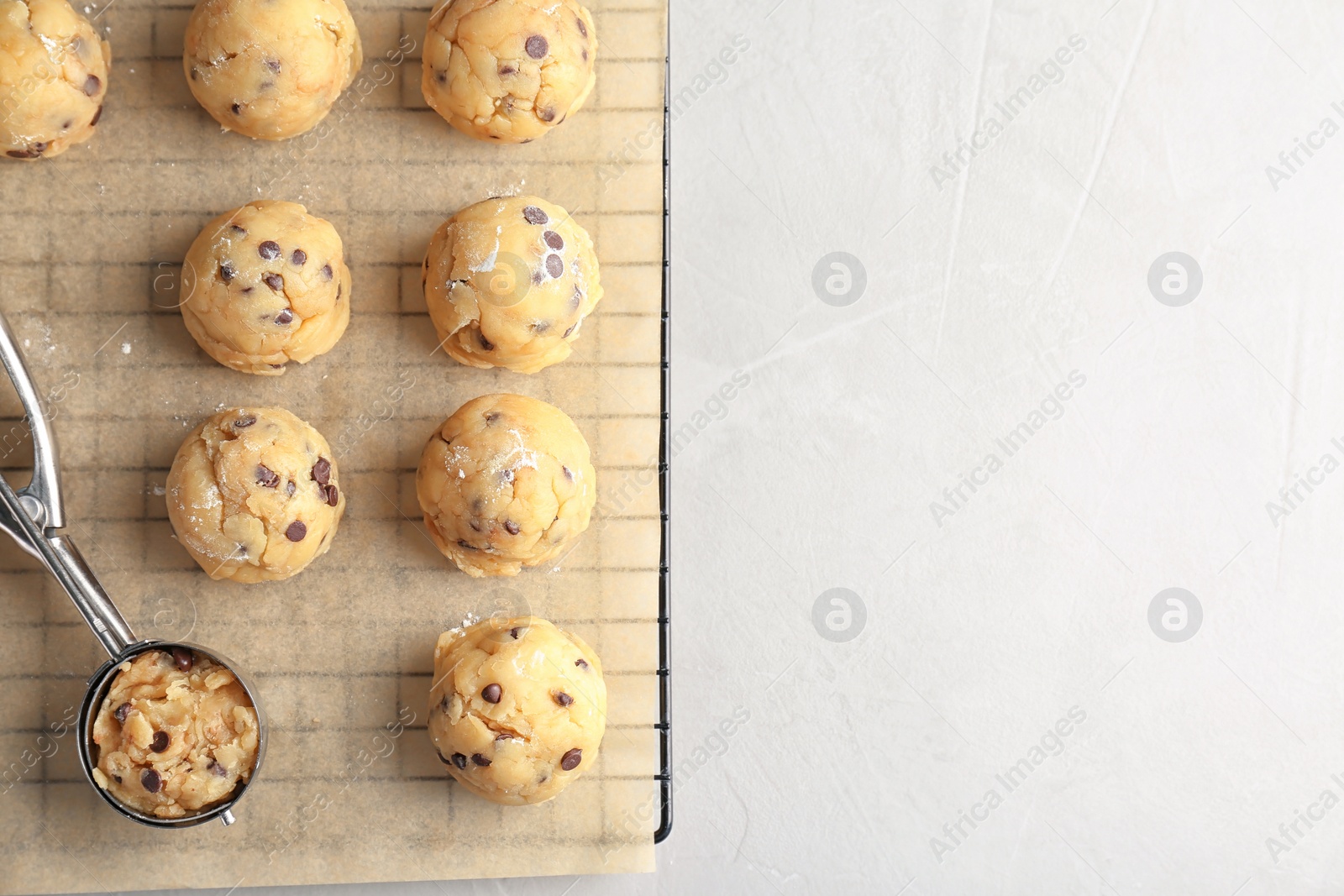 Photo of Raw cookie dough with chocolate chips and scoop on parchment paper, top view