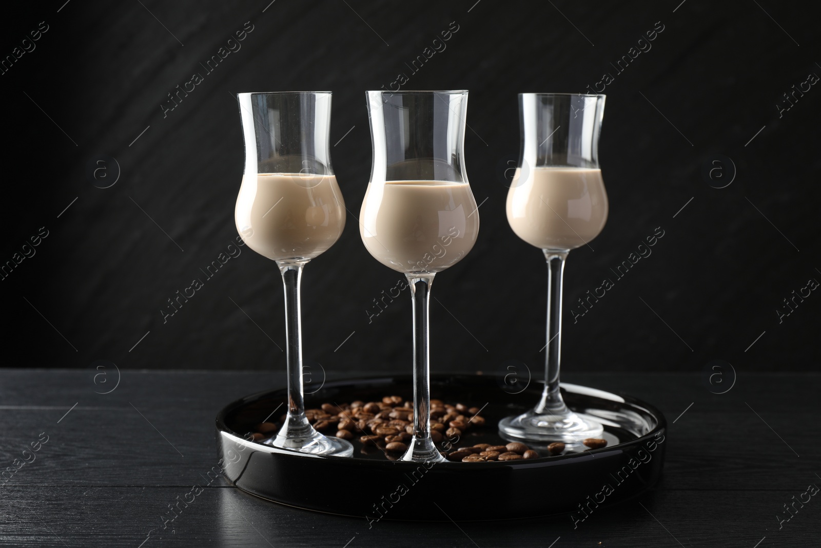 Photo of Coffee cream liqueur in glasses and beans on black wooden table