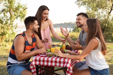 Happy young people having picnic at table in park