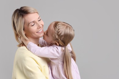Photo of Daughter kissing her happy mother on grey background. Space for text