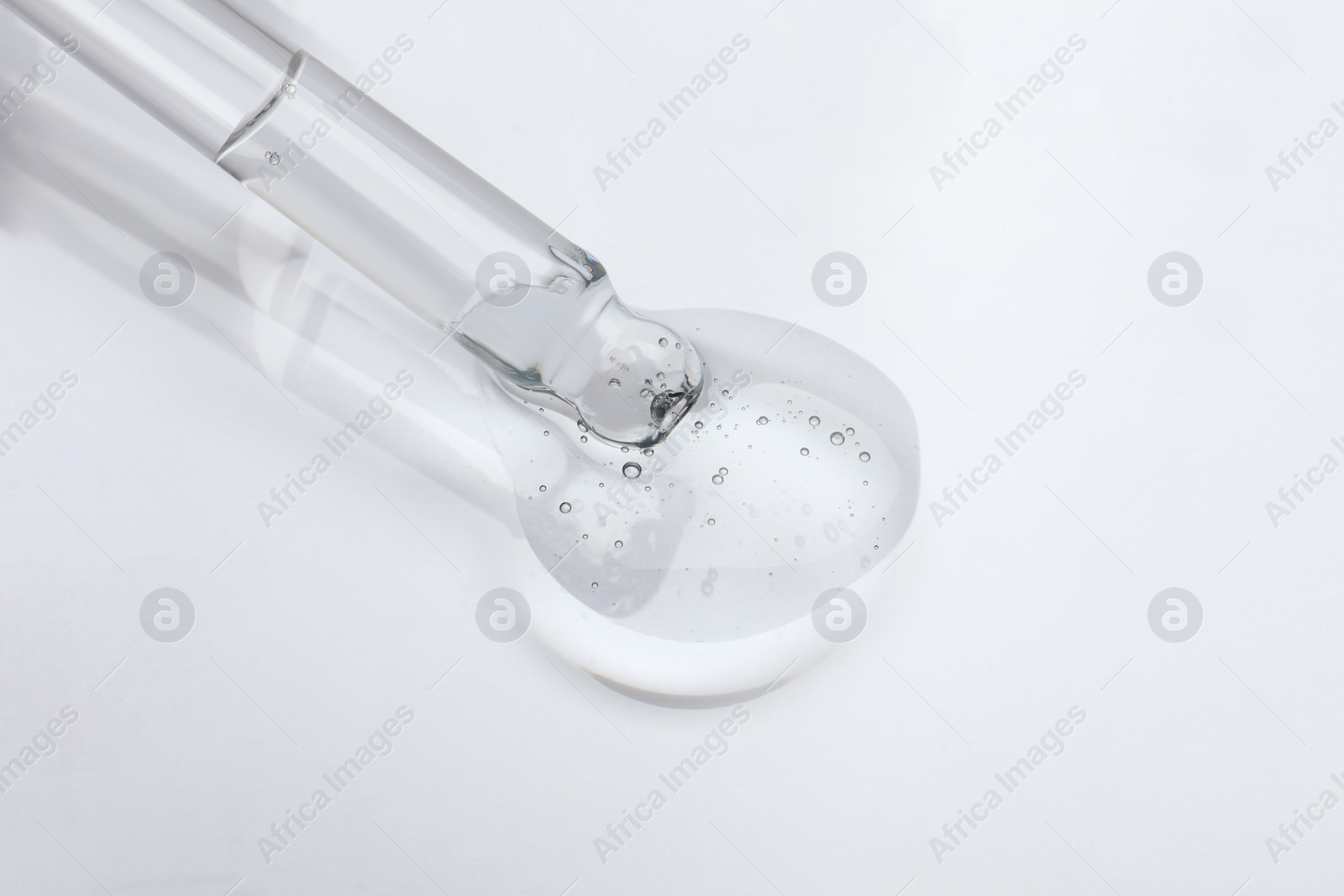 Photo of Dripping cosmetic oil from pipette onto light surface, closeup