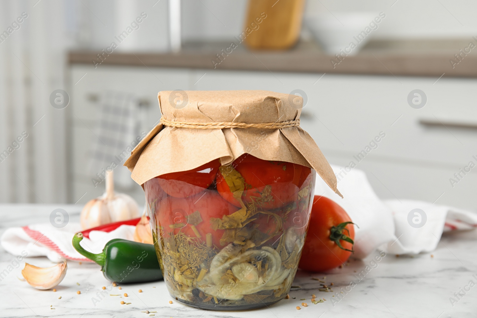 Photo of Pickled tomatoes in glass jar and products on white marble table in kitchen