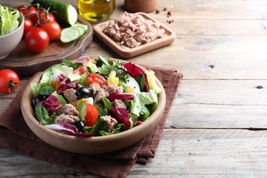 Photo of Bowl of delicious salad with canned tuna and vegetables on wooden table, space for text