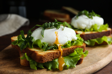 Delicious poached egg sandwich served on wooden board, closeup