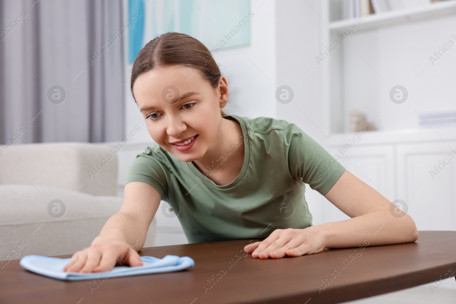 Photo of Woman with microfiber cloth cleaning wooden table in room