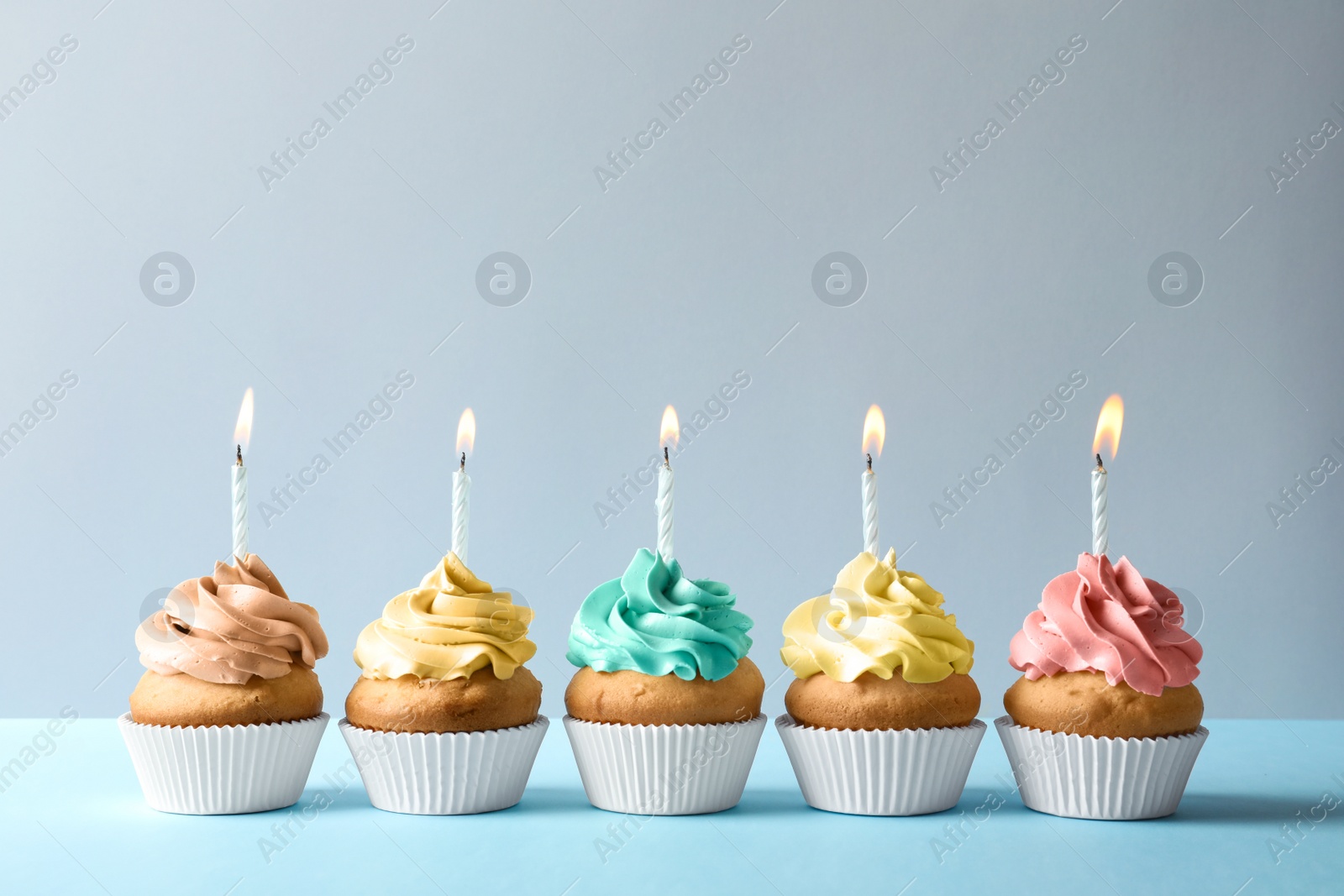 Photo of Delicious birthday cupcakes with candles on light background