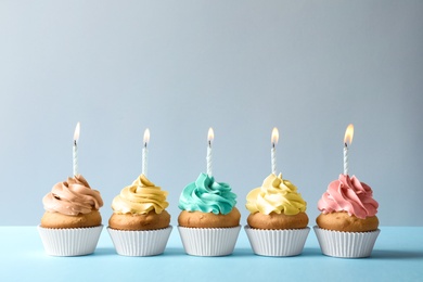 Delicious birthday cupcakes with candles on light background