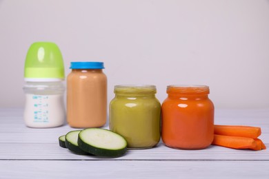 Healthy baby food, bottle with milk and fresh vegetables on white wooden table