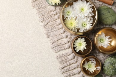 Photo of Tibetan singing bowls with water, beautiful chrysanthemum flowers and stones on table, flat lay. Space for text