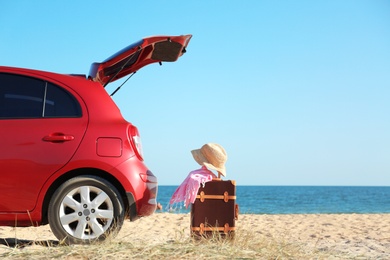 Photo of Modern car, retro suitcase and beach accessories on sand near sea. Space for text