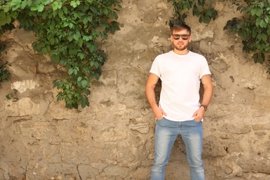 Photo of Young man wearing white t-shirt near stone wall on street