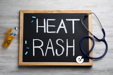 Photo of Blackboard with words Heat Rash, stethoscope and pills on wooden table, flat lay