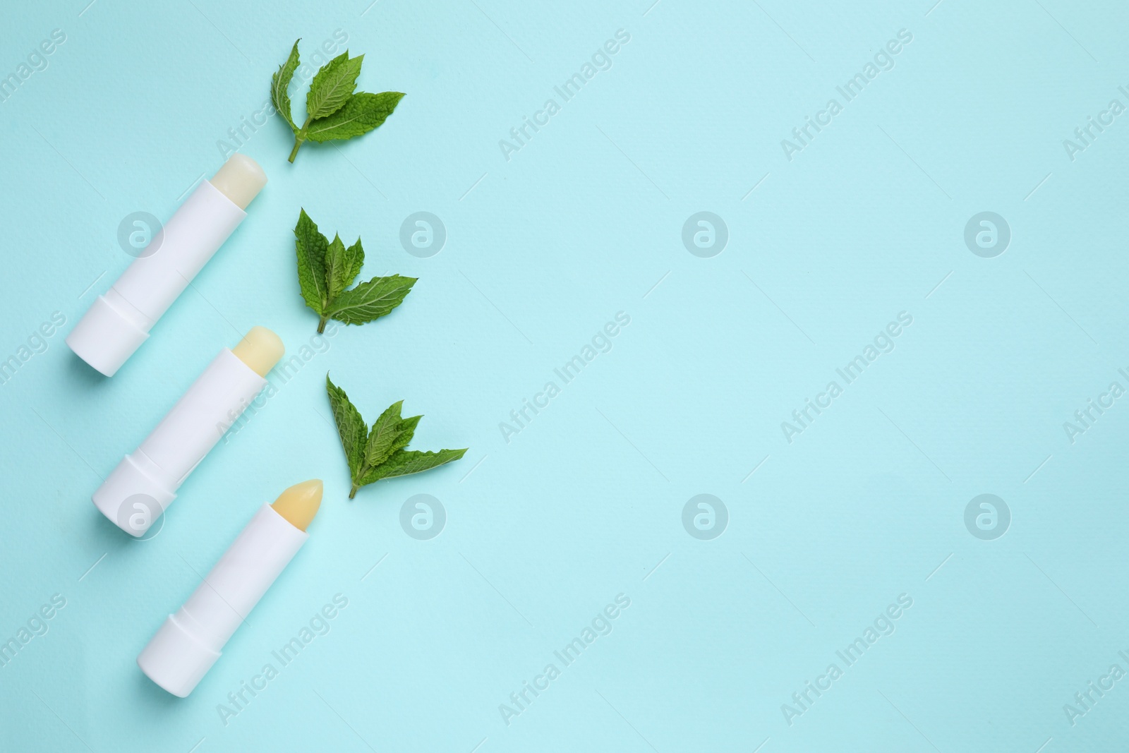 Photo of Hygienic lipsticks and mint leaves on turquoise background, flat lay. Space for text