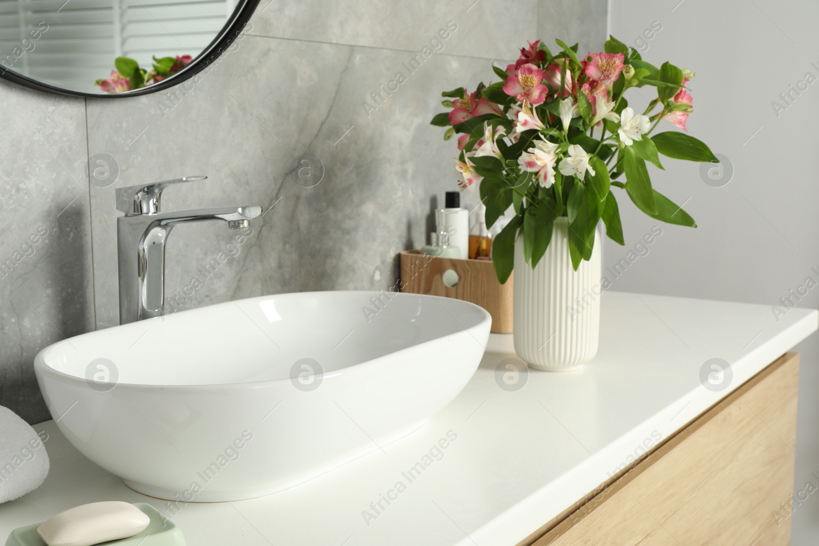 Photo of Vase with beautiful Alstroemeria flowers and toiletries near sink in bathroom