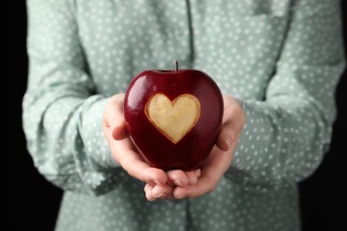Photo of Woman holding red apple with carved heart on black background, closeup