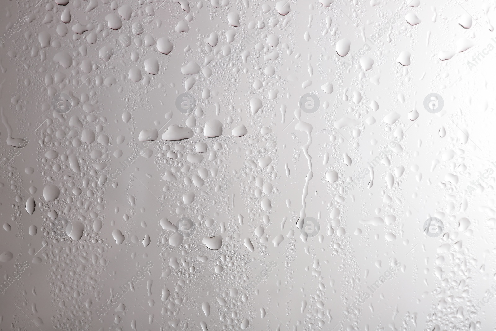 Photo of Glass with rain drops against light background