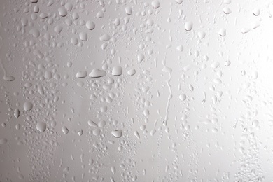 Photo of Glass with rain drops against light background