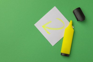 Photo of Bright yellow marker and sticky note with drawn arrow on green background, flat lay. Space for text