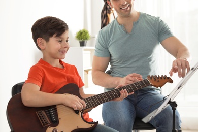 Little boy playing guitar with his teacher at music lesson. Learning notes