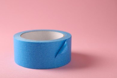 Photo of Roll of light blue adhesive tape on pink background. Space for text