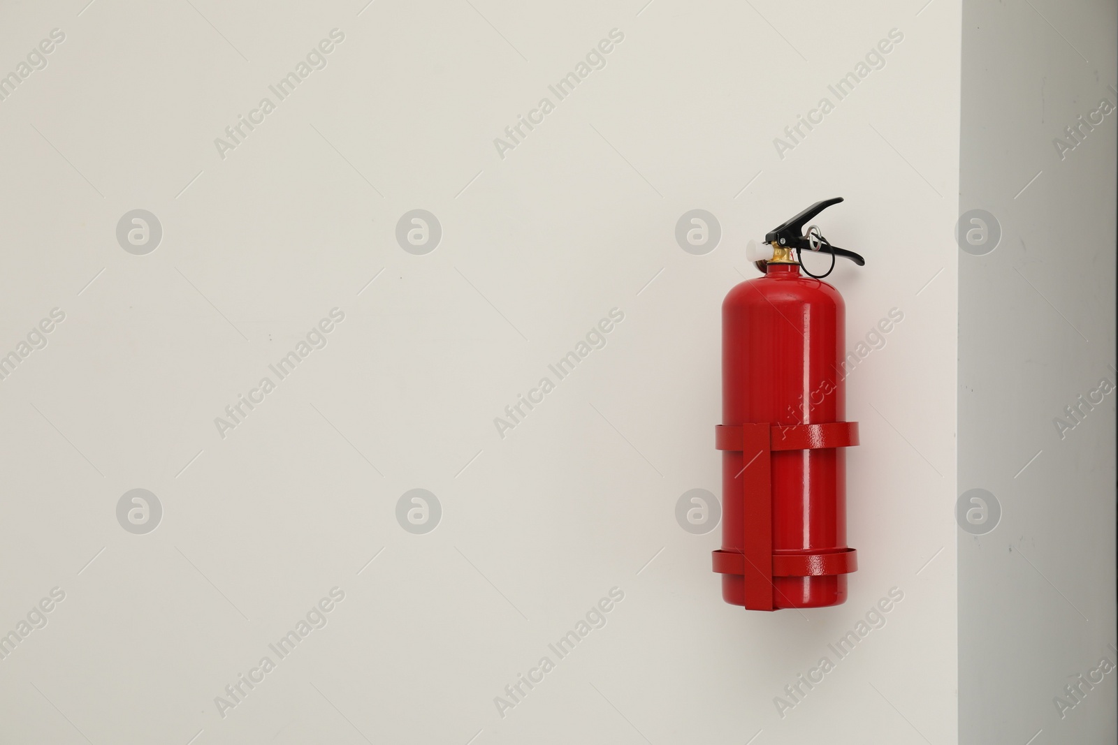 Photo of Fire extinguisher on light wall, space for text