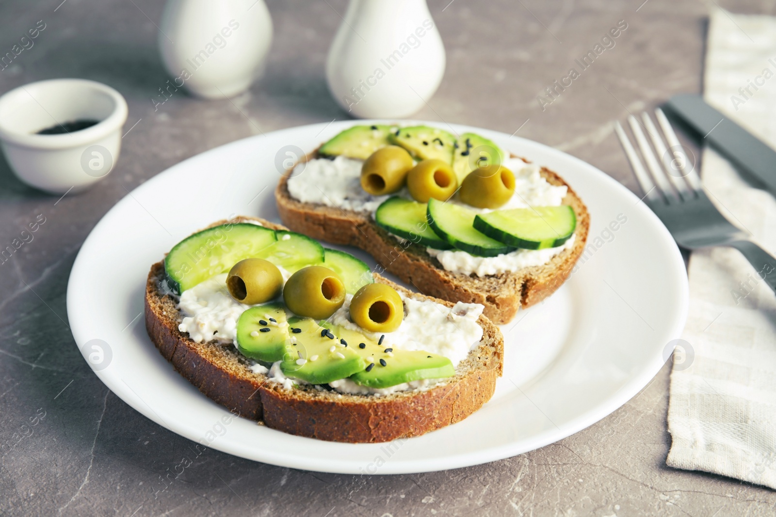 Photo of Crisp rye toasts with sliced avocado, cream cheese and olives on plate, closeup