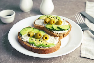 Photo of Crisp rye toasts with sliced avocado, cream cheese and olives on plate, closeup