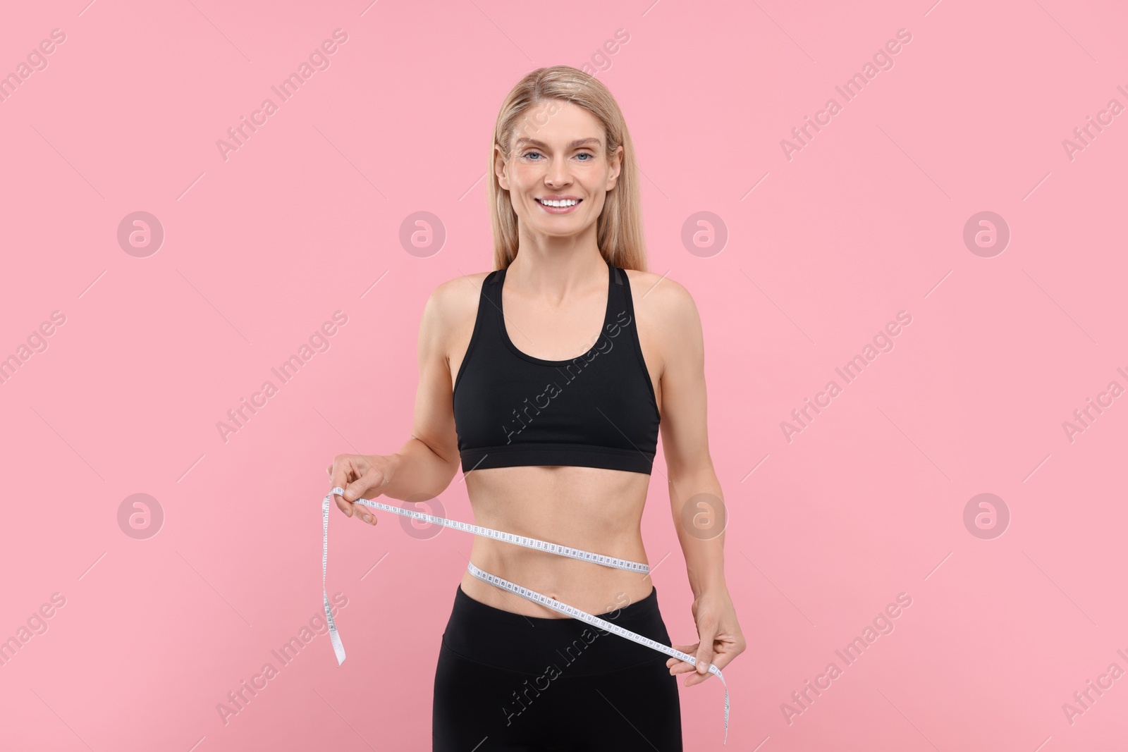 Photo of Slim woman measuring waist with tape on pink background. Weight loss