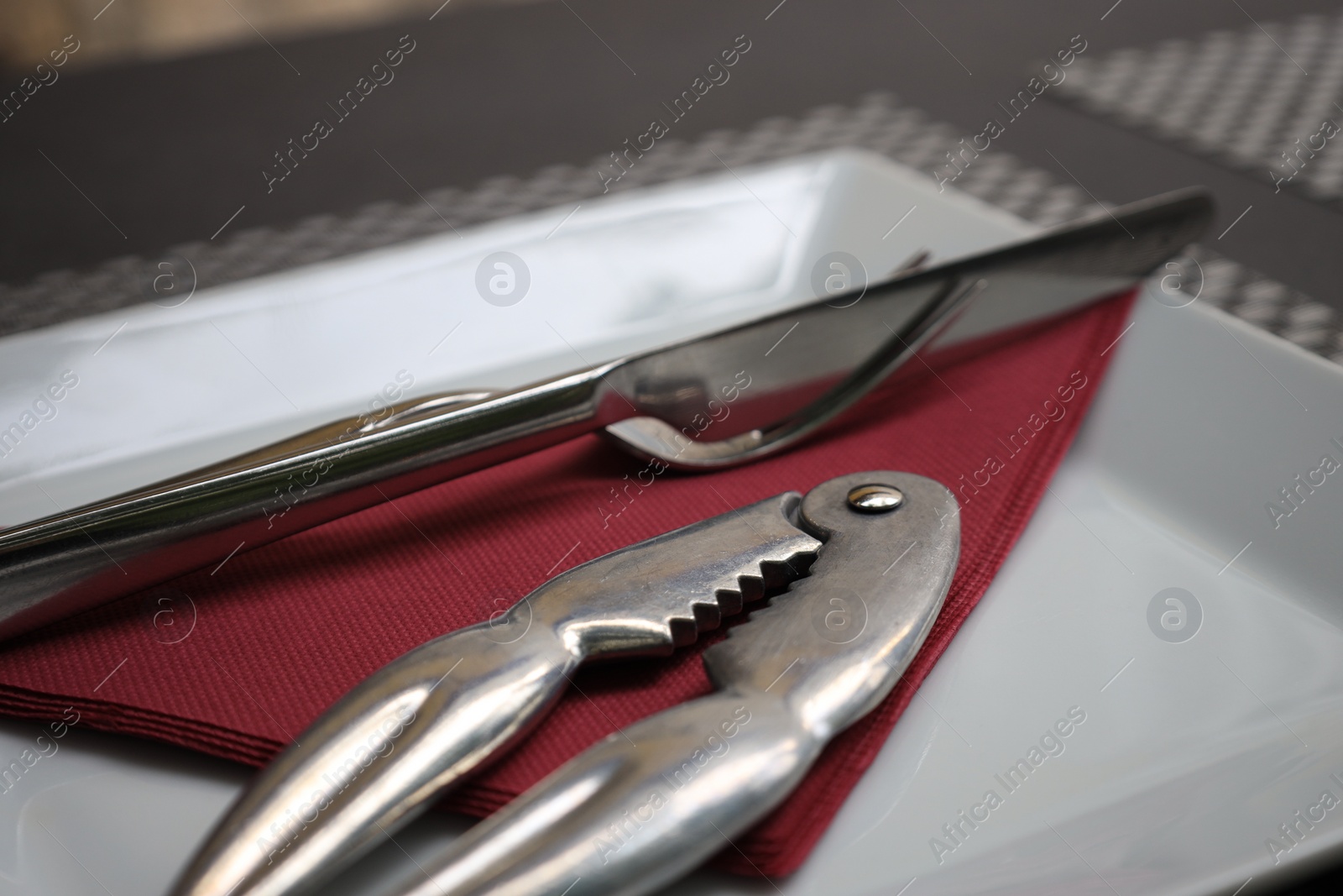 Photo of Plate, napkin, cutlery and lobster cracker on black table, closeup