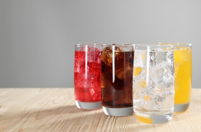 Photo of Glasses of different refreshing soda water with ice cubes on wooden table, space for text