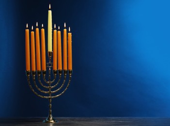 Hanukkah celebration. Menorah with burning candles on table against blue background, space for text