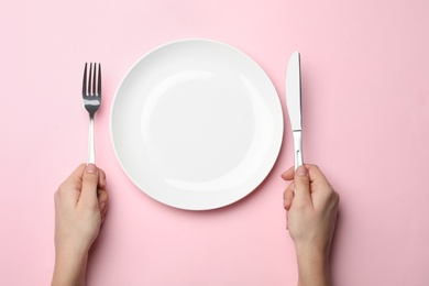 Photo of Woman with fork, knife and empty plate on color background, top view