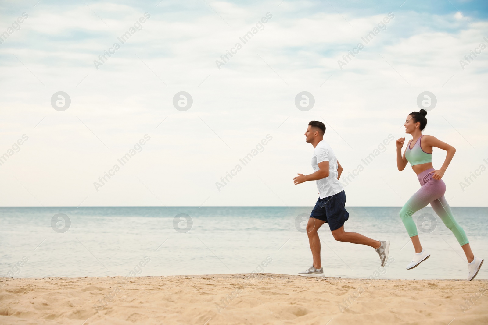 Photo of Couple running together on beach, space for text. Body training