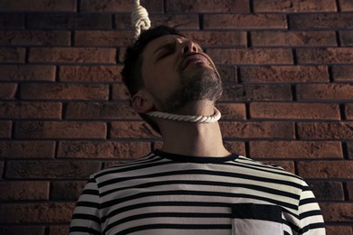 Depressed man with rope noose on neck near brick wall, low angle view