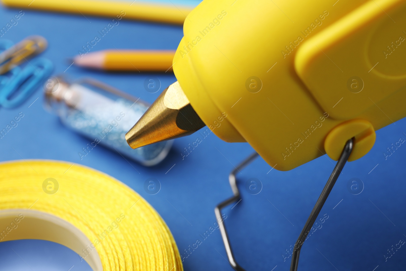 Photo of Hot glue gun and handicraft materials on blue table, closeup